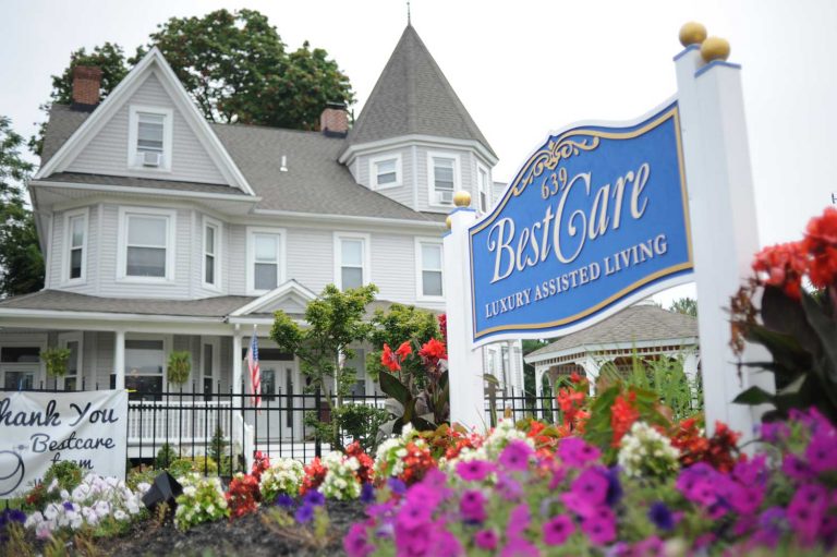 BestCare Luxury Assisted Living sign with a large Victorian-style facility and flower garden in the background