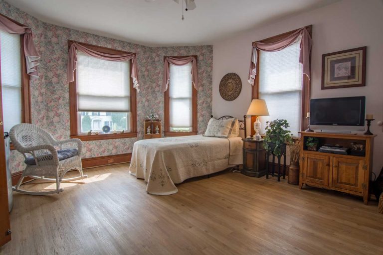 Spacious bedroom with a single bed, rocking chair, and floral wallpaper in an assisted living facility