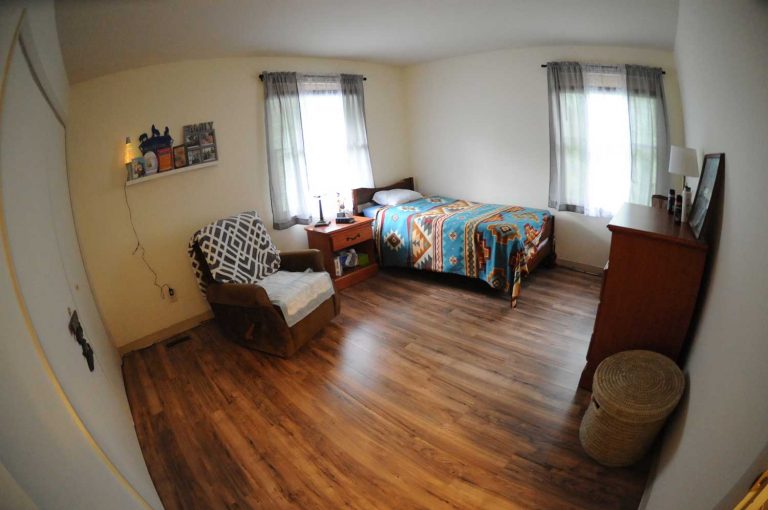 Spacious bedroom in an assisted living facility with a single bed, armchair, and wooden flooring