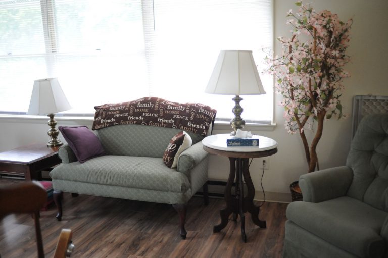 Cozy living room area with a couch, table, and decorative lamp in an assisted living facility.